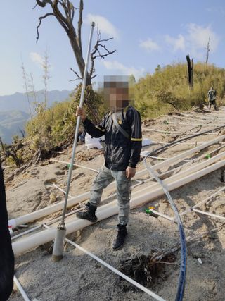 A rare earth miner stands on a network of pipes used to inject chemicals into a hillside in Kachin State, Myanmar